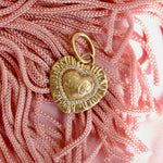 Gold heart-shaped pendant with 'SC' initials on a pink textured background
